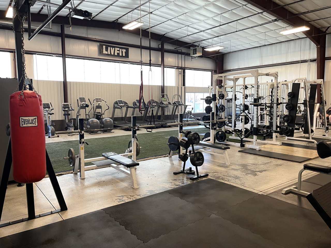Wide view of the gym with punching bag, cardio machines, and squat racks.